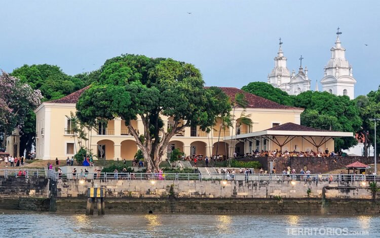 Casa colonial com jardim onde pessoas sentam. Catedral de Belém ao fundo