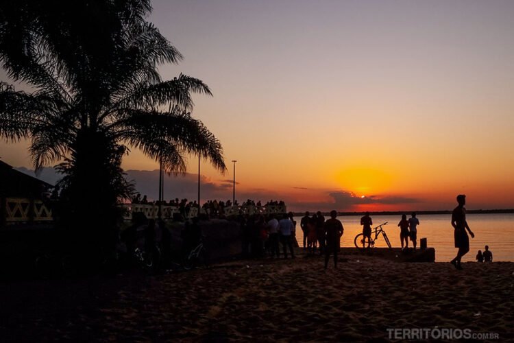 Pôr do sol em praia com palmeira, silhueta de pessoas