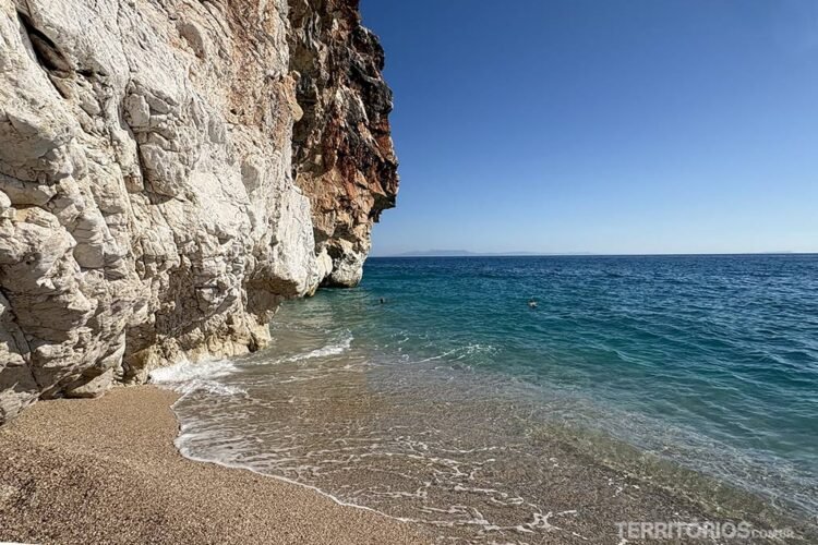 Mar turquesa e céu azul, água bate nas rochas brancas e areia