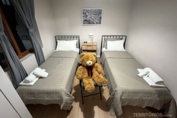 Quarto em casa por temporada na Albânia com duas camas de solteiro, cortinas, urso de pelúcia, tolhas e quadro na parede.