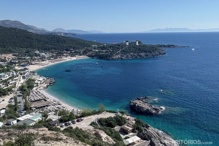 Vista para uma praia de mar azul na Albânia com rochas e muitas construções