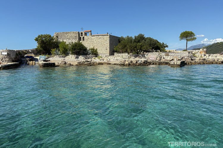 Mosteiro de pedra antigo em ilha na Baía de Kotor, Mar em tom de verde transparente e céu azul