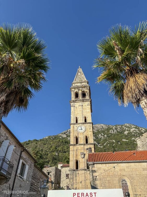 Torre de igreja medieval em palmeiras, montanha e céu azul