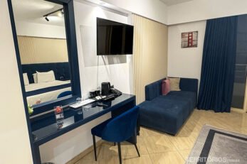 Quarto de hotel na Albânia com sofá e sacada. TV, mesa e espelho refletindo cama.