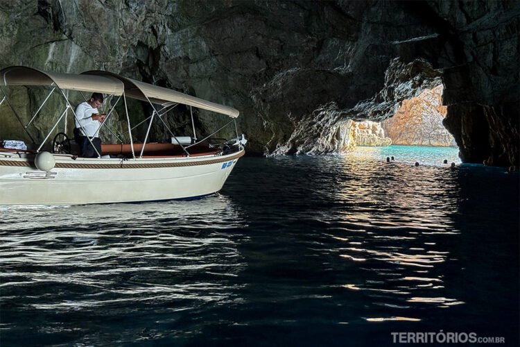 Interior de uma caverna no mar com lancha parada e luz entrando.