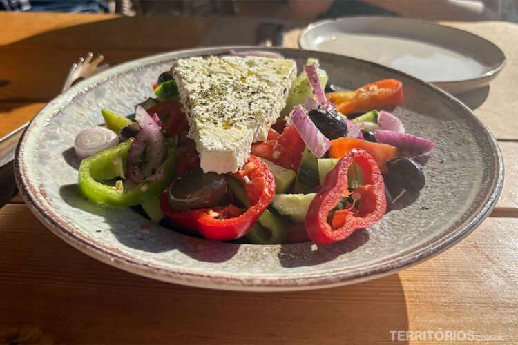 Prato servido com salada grega e queijo branco. Sol ilumina mesa.