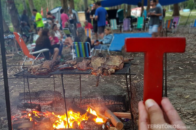 Tesão no Uruguai: letra vermelha de madeira em frente a parrilla de acampamento e pessoas interagindo sentada em cadeiras