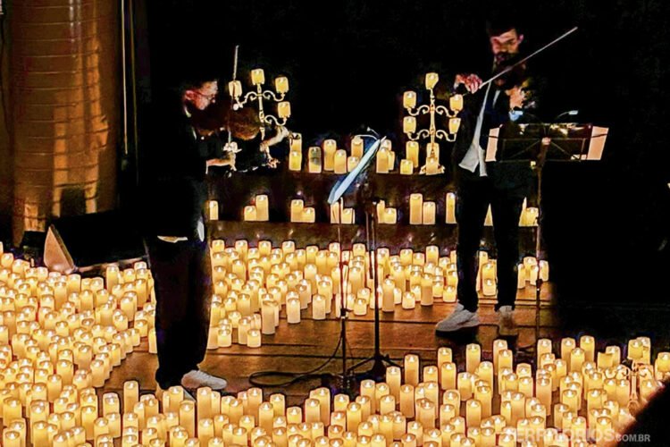 Dois músicos violinistas se apresentam no palco entre as velas do espetáculo Candlelight