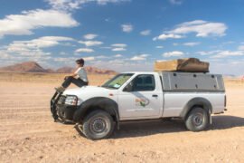 Mulher posa em cima do capô da caminhonete 4x4 durante a viagem pela Namíbia de carro